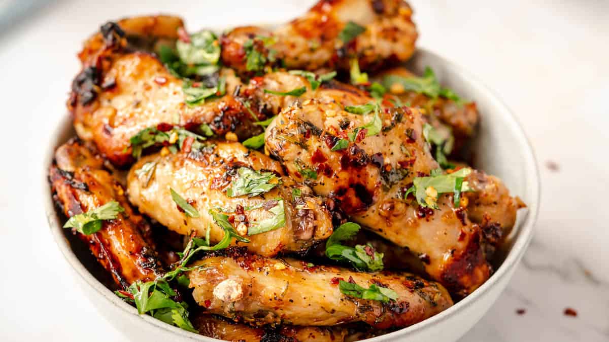 A bowl filled with grilled chicken wings garnished with chopped herbs and seasoning.