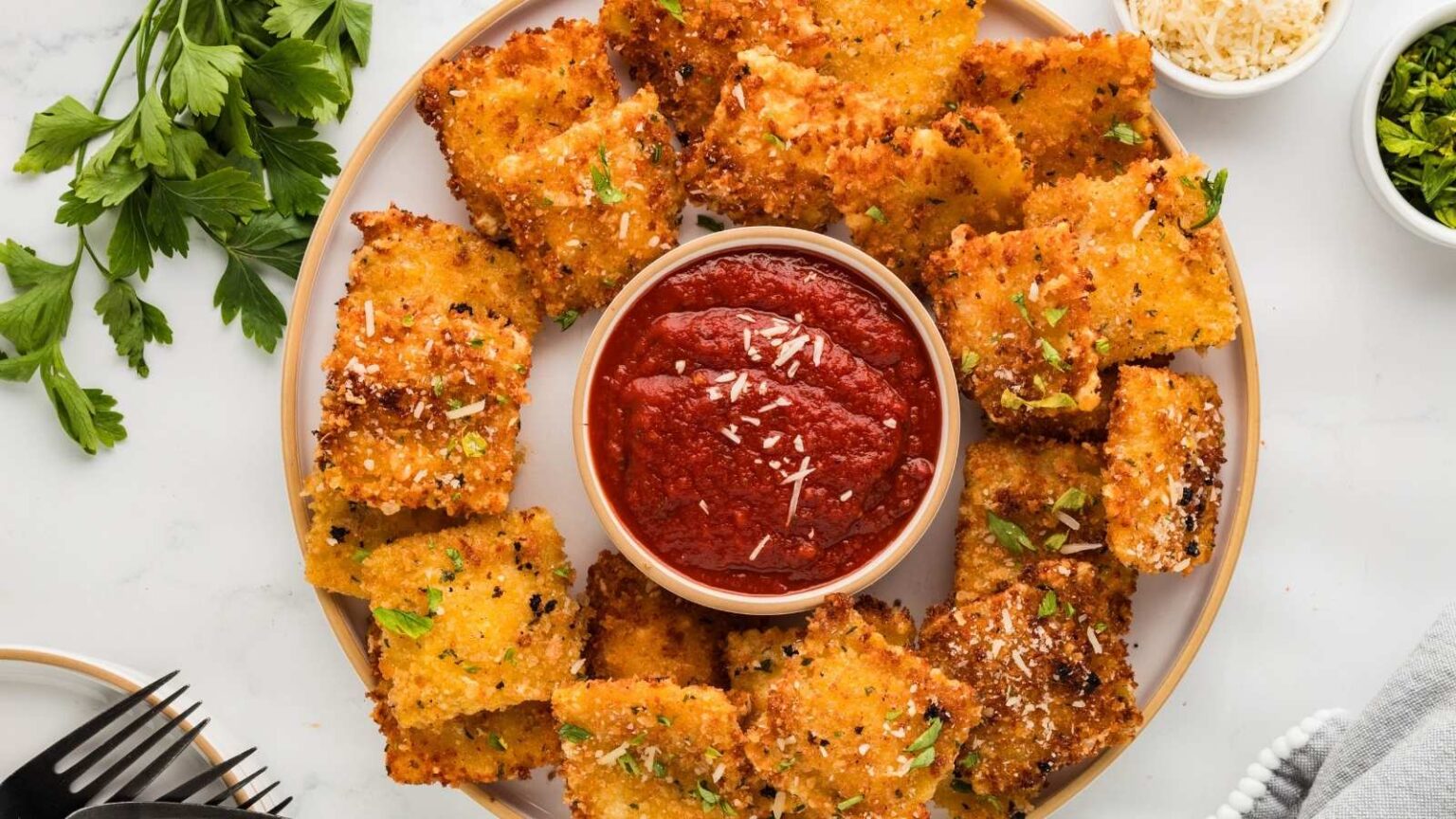 A plate of breaded and fried ravioli arranged around a bowl of marinara sauce, garnished with chopped herbs and grated cheese.