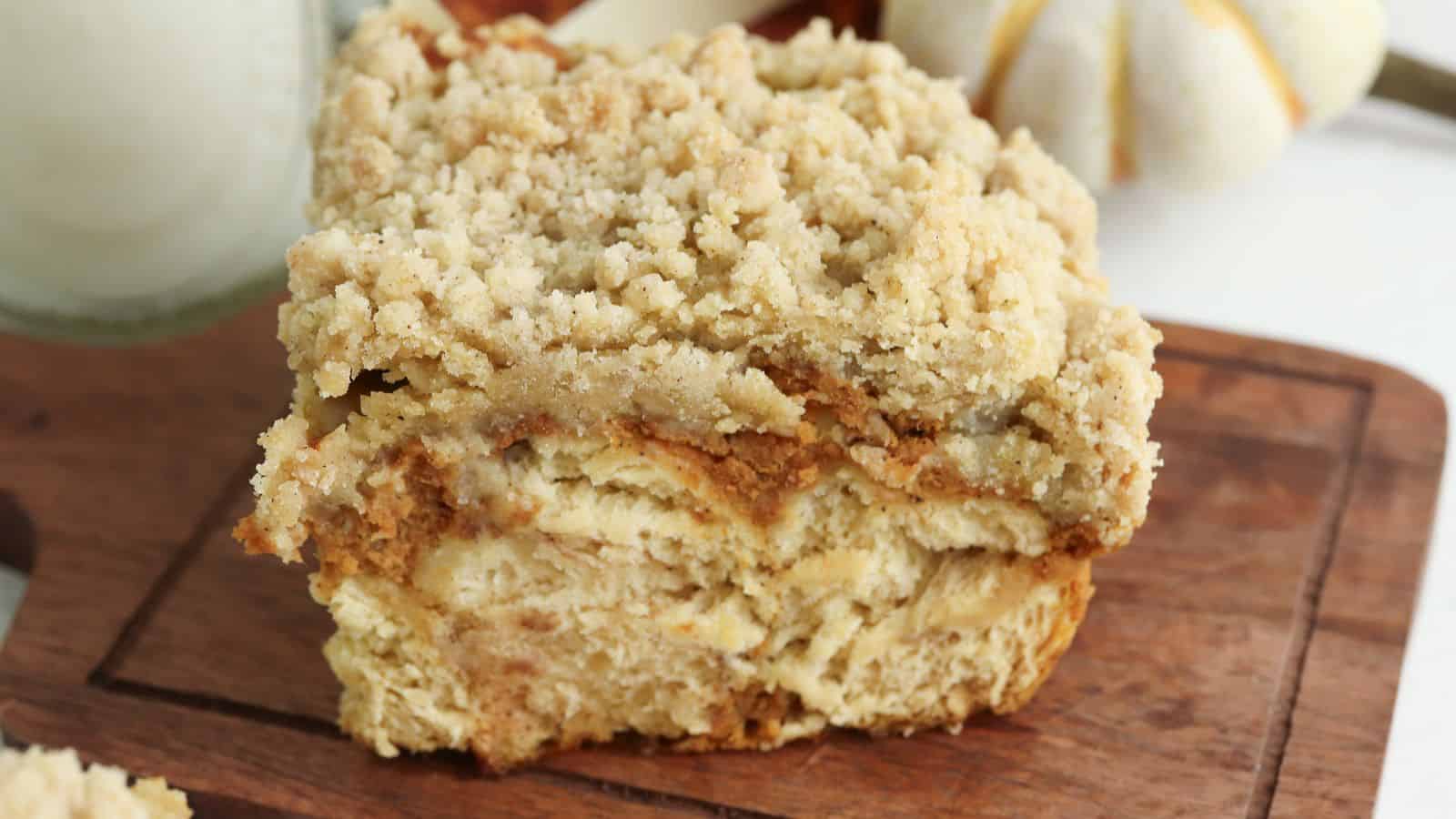 A close-up of a slice of crumb cake with a crumbly topping, resting on a wooden cutting board.