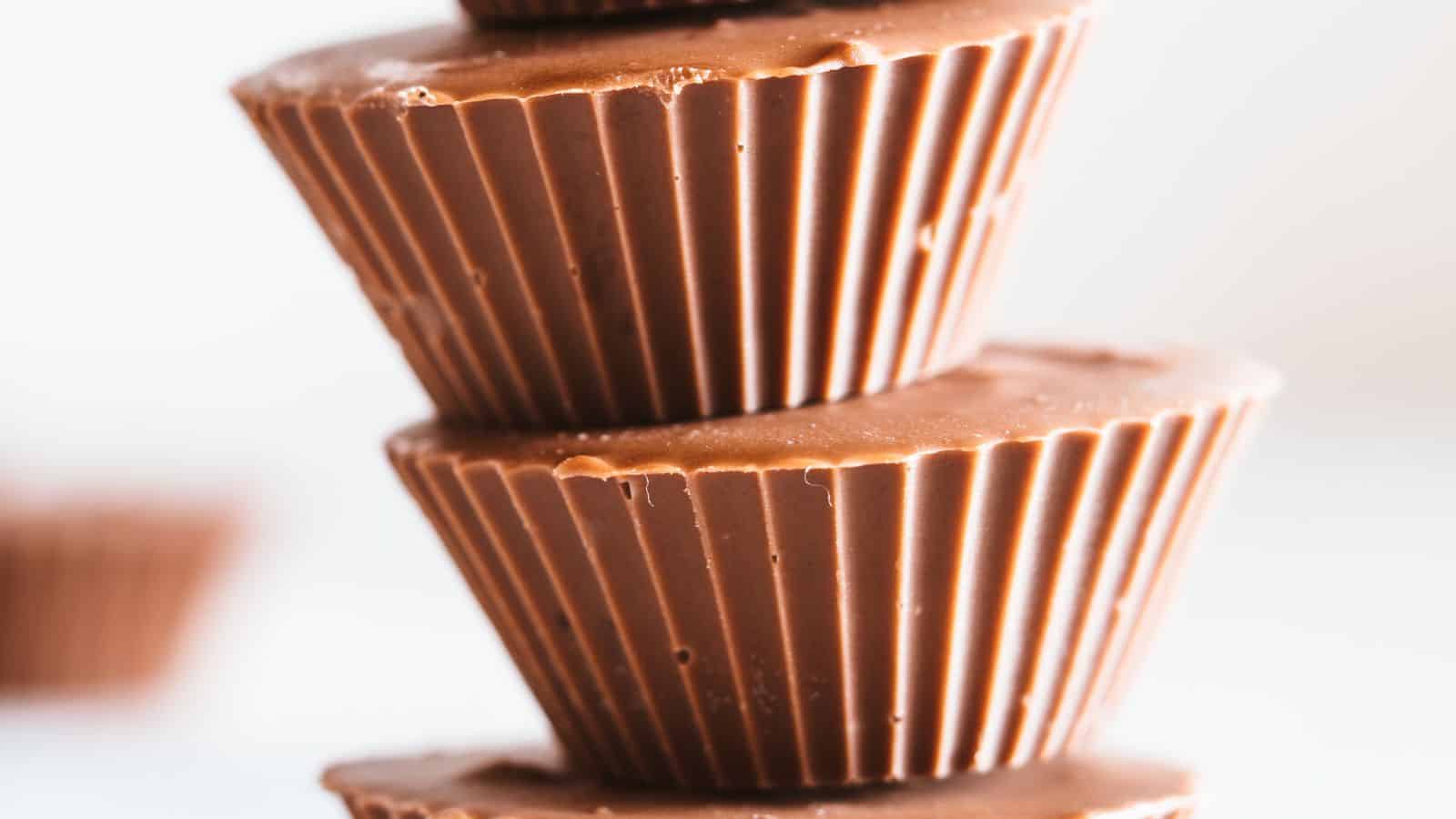 A close-up of a stacked pile of chocolate cups, each with ridged sides and smooth tops, against a plain background.