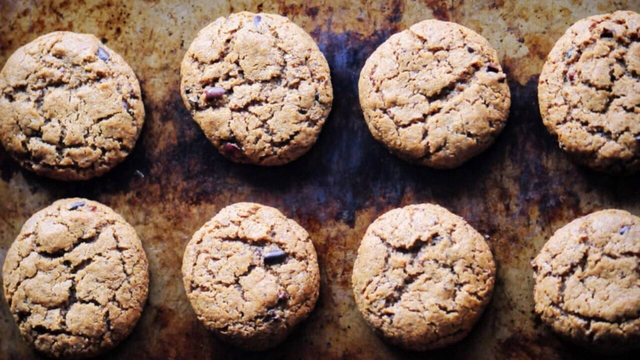 Eight round cookies are arranged in two neat rows on a baking sheet with a brown, slightly worn surface.