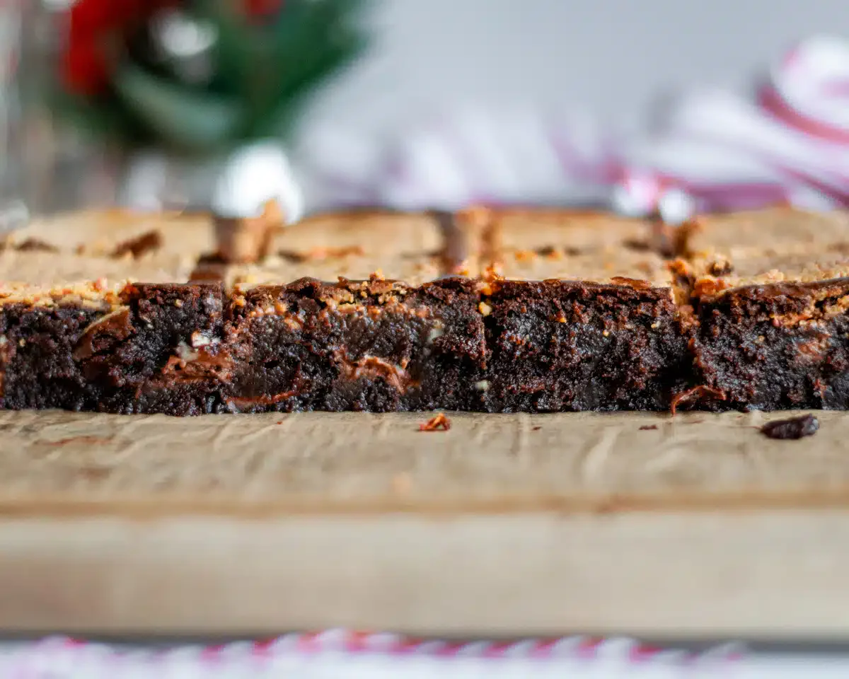 A close-up of sliced brownies on a wooden cutting board, showing a dense, fudgy texture and a slightly crisp top.