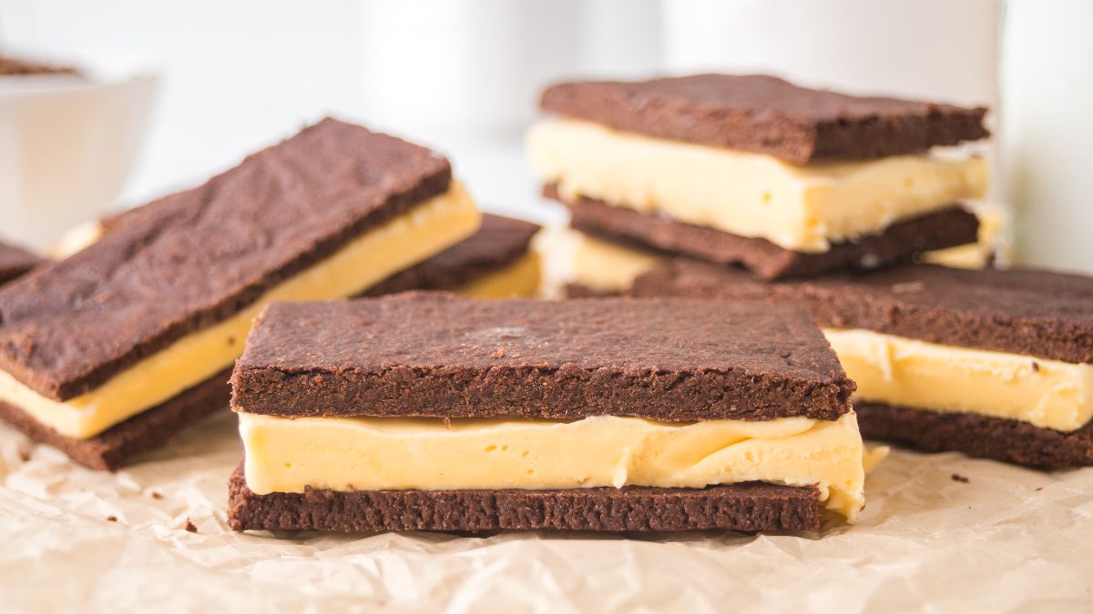 Several chocolate ice cream sandwiches with vanilla filling are arranged on brown parchment paper.