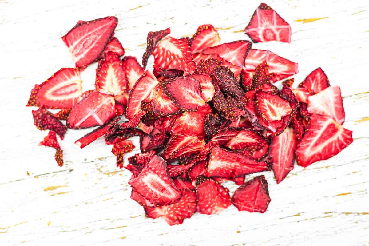 A pile of dried, sliced strawberries is spread out on a white wooden surface.