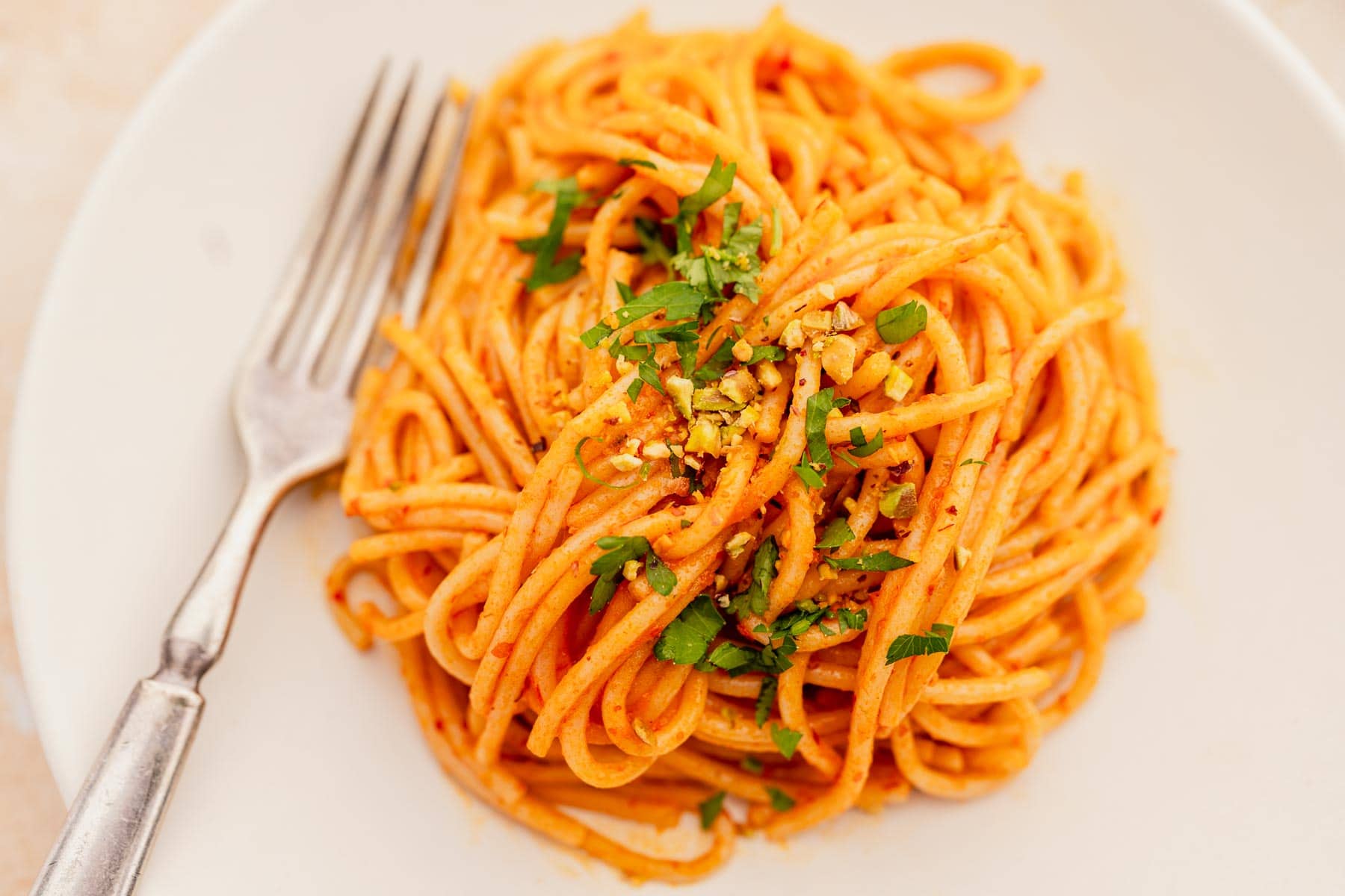 A plate of spaghetti with red sauce, garnished with chopped herbs and crushed nuts, next to a fork.