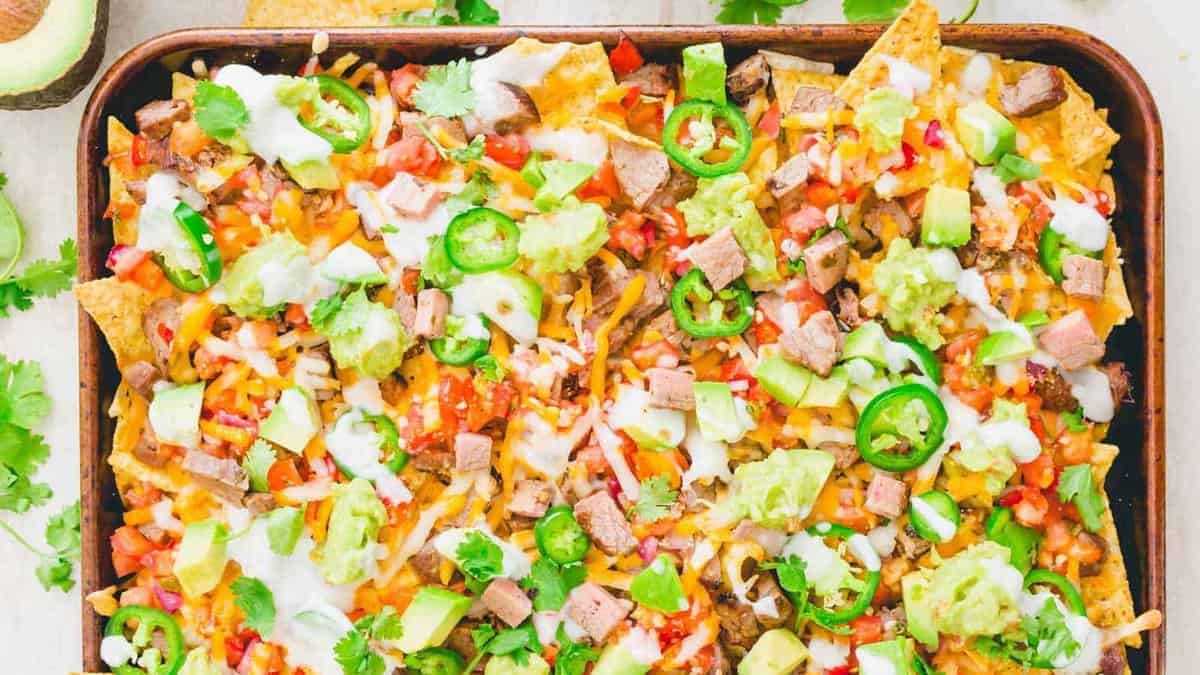 A tray of loaded nachos topped with diced steak, melted cheese, jalapeรฑos, guacamole, sour cream, pico de gallo, and fresh cilantro.