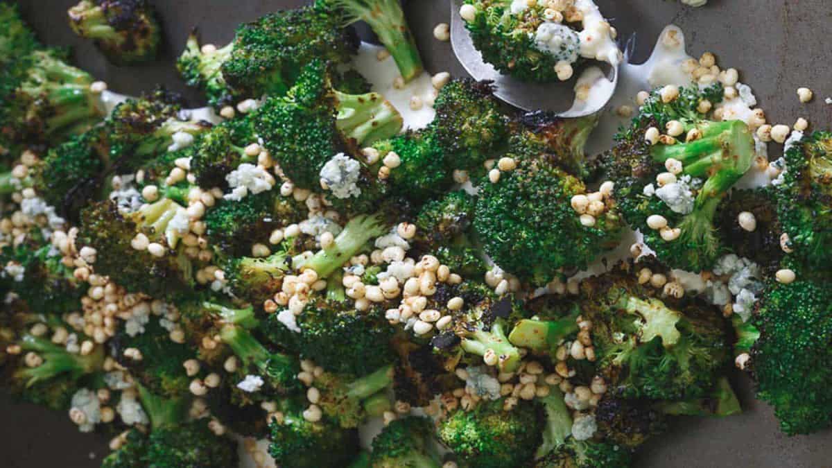 Roasted broccoli florets topped with blue cheese crumbles, toasted puffed grains, and a drizzle of creamy sauce on a dark surface.