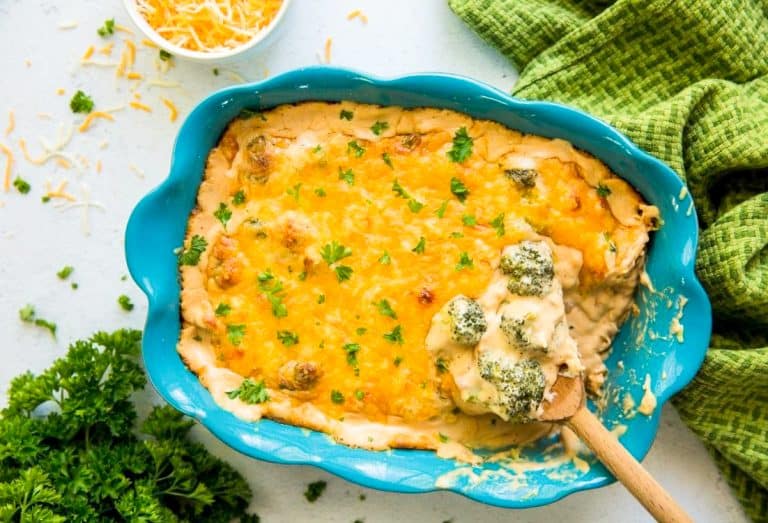 A blue baking dish filled with cheesy broccoli casserole, topped with melted cheese and parsley, with a wooden spoon scooping out a serving.