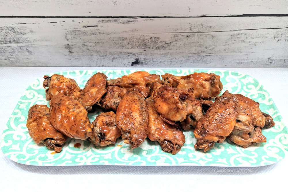 A rectangular plate with several cooked chicken wings covered in a brown glaze, arranged in rows on a patterned teal and white platter.