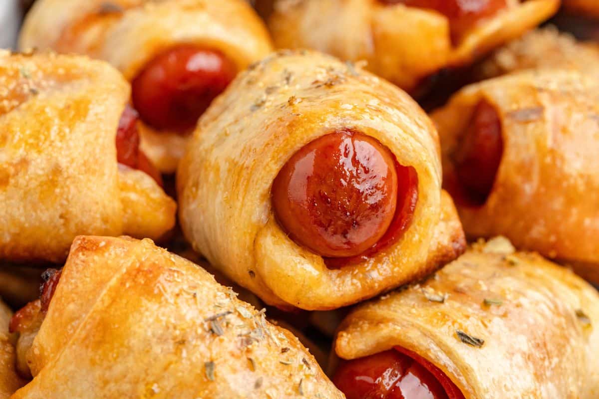 Close-up of several pigs in a blanket, showing mini sausages wrapped in golden-brown, seasoned pastry.
