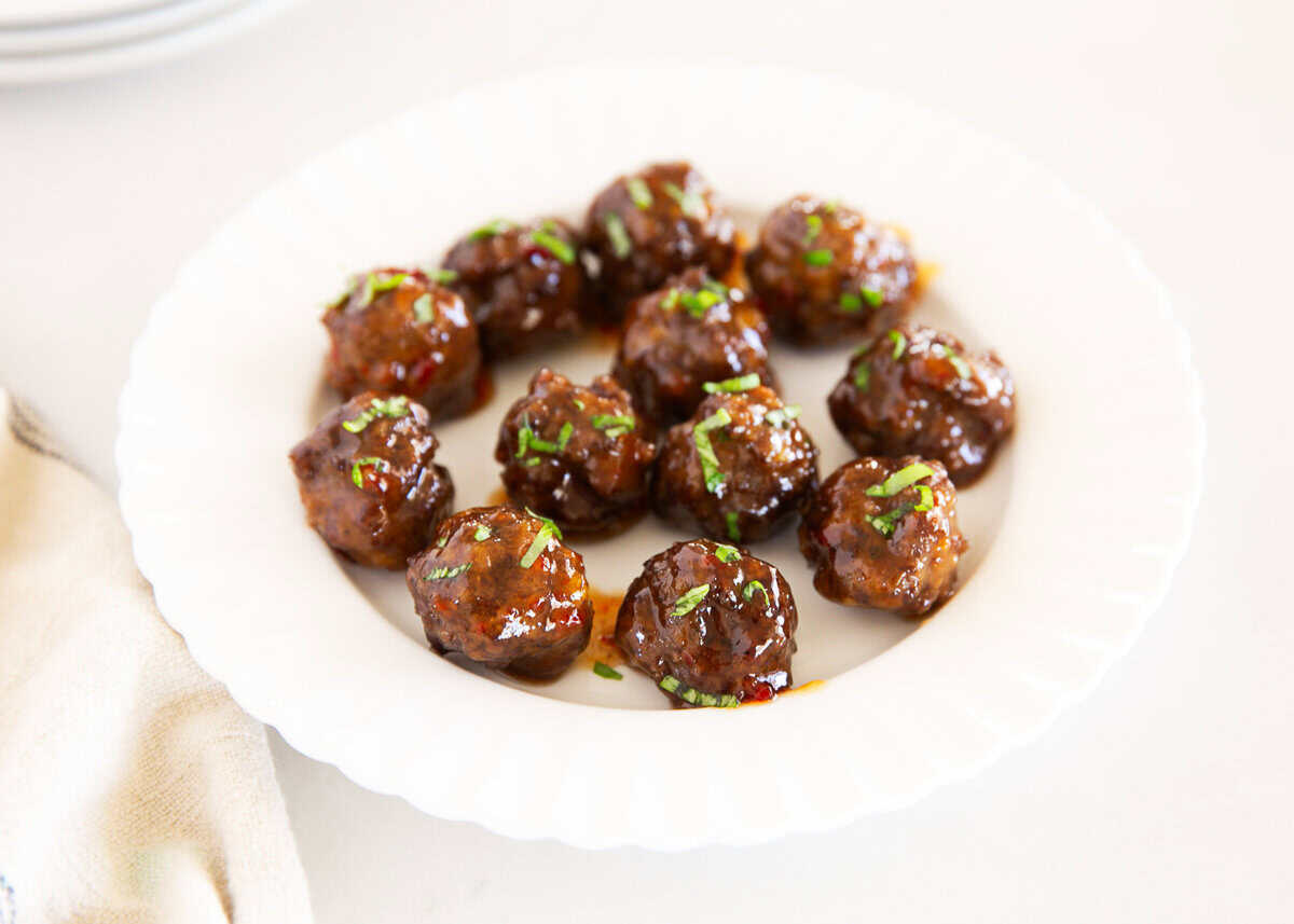 A white plate with glazed meatballs garnished with chopped herbs, arranged in a circular pattern on a light surface.