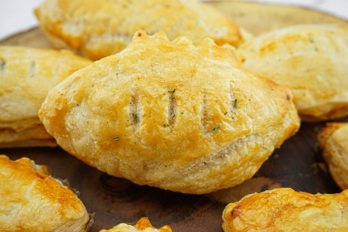 Golden-brown, flaky puff pastry turnovers with a crimped edge and a few slits on top, arranged on a wooden surface.