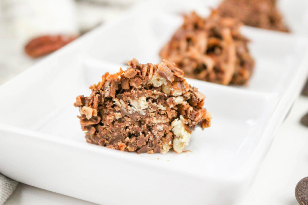 A close-up of a chocolate and nut cluster dessert on a white rectangular plate, with another similar dessert in the background.