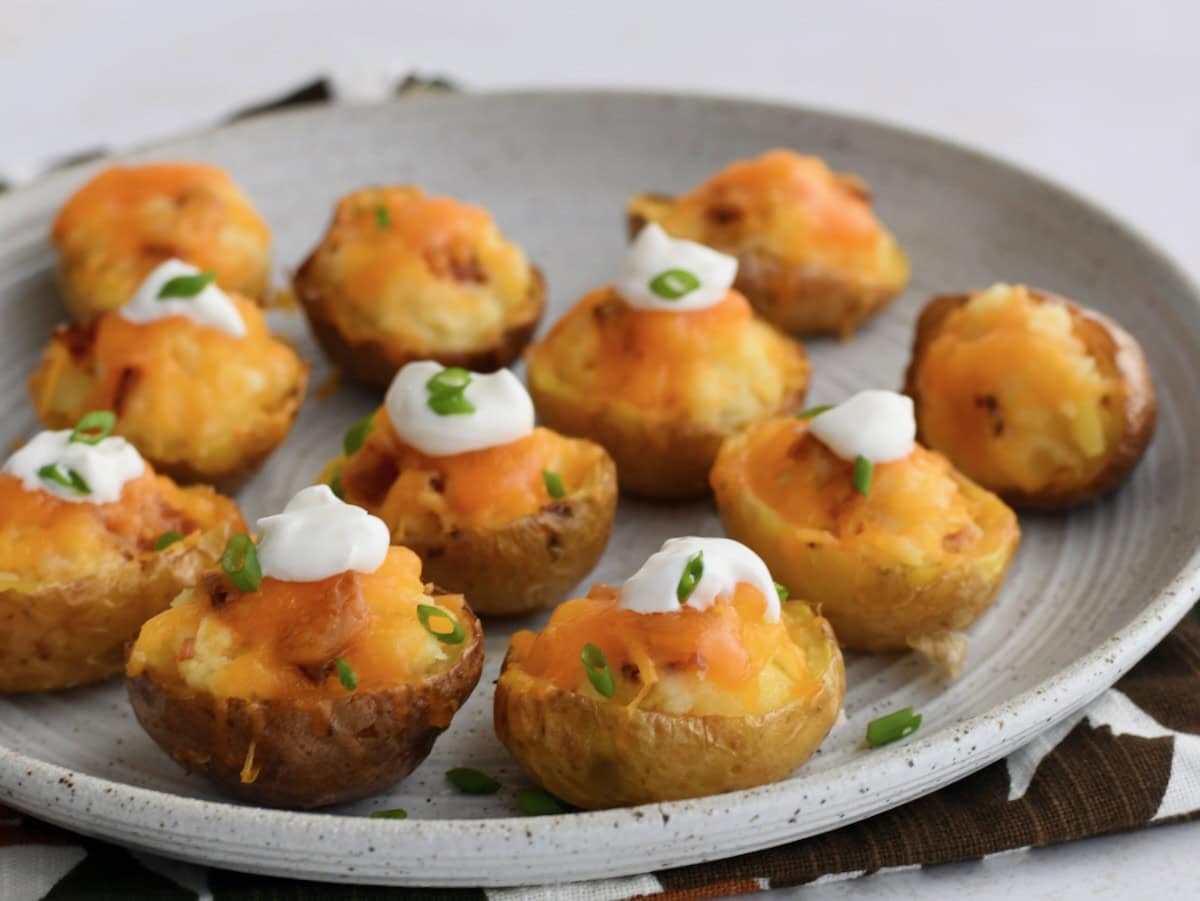 A plate of twice-baked potato halves topped with melted cheese, sour cream, and chopped green onions, arranged on a gray dish.