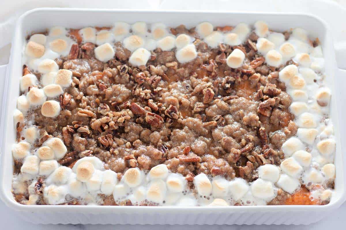 A baked sweet potato casserole topped with toasted marshmallows, chopped pecans, and a crumbly brown sugar streusel in a white rectangular dish.