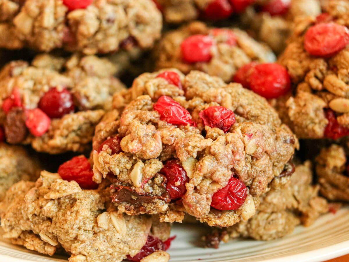 Close-up of several oatmeal cookies with visible red cranberries and oats, stacked on a plate.