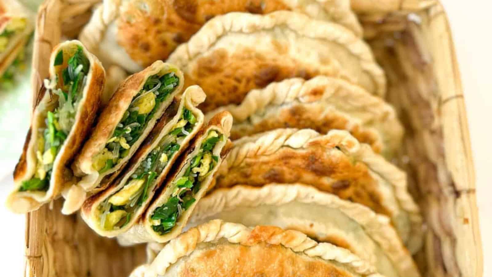A basket filled with several folded, golden-brown pastries, some sliced open to reveal a green vegetable filling.