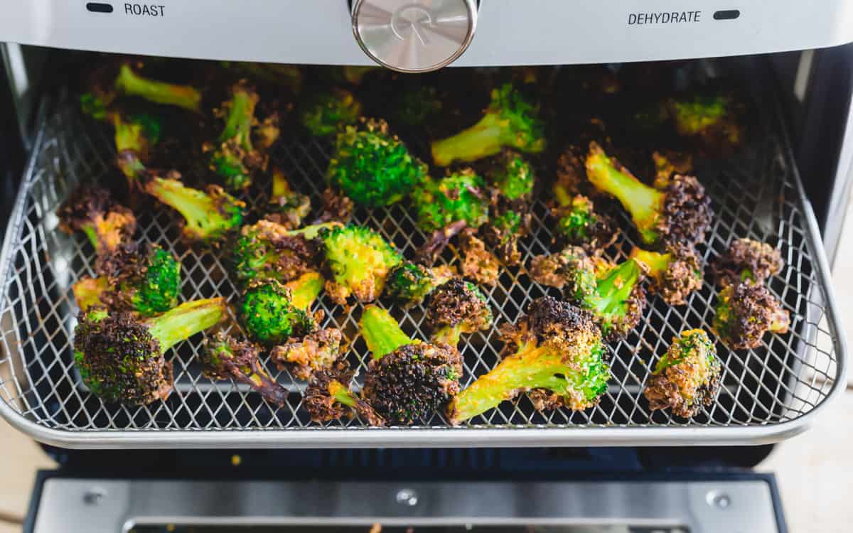 Broccoli florets are being roasted in an air fryer tray, showing a mix of green and browned edges.