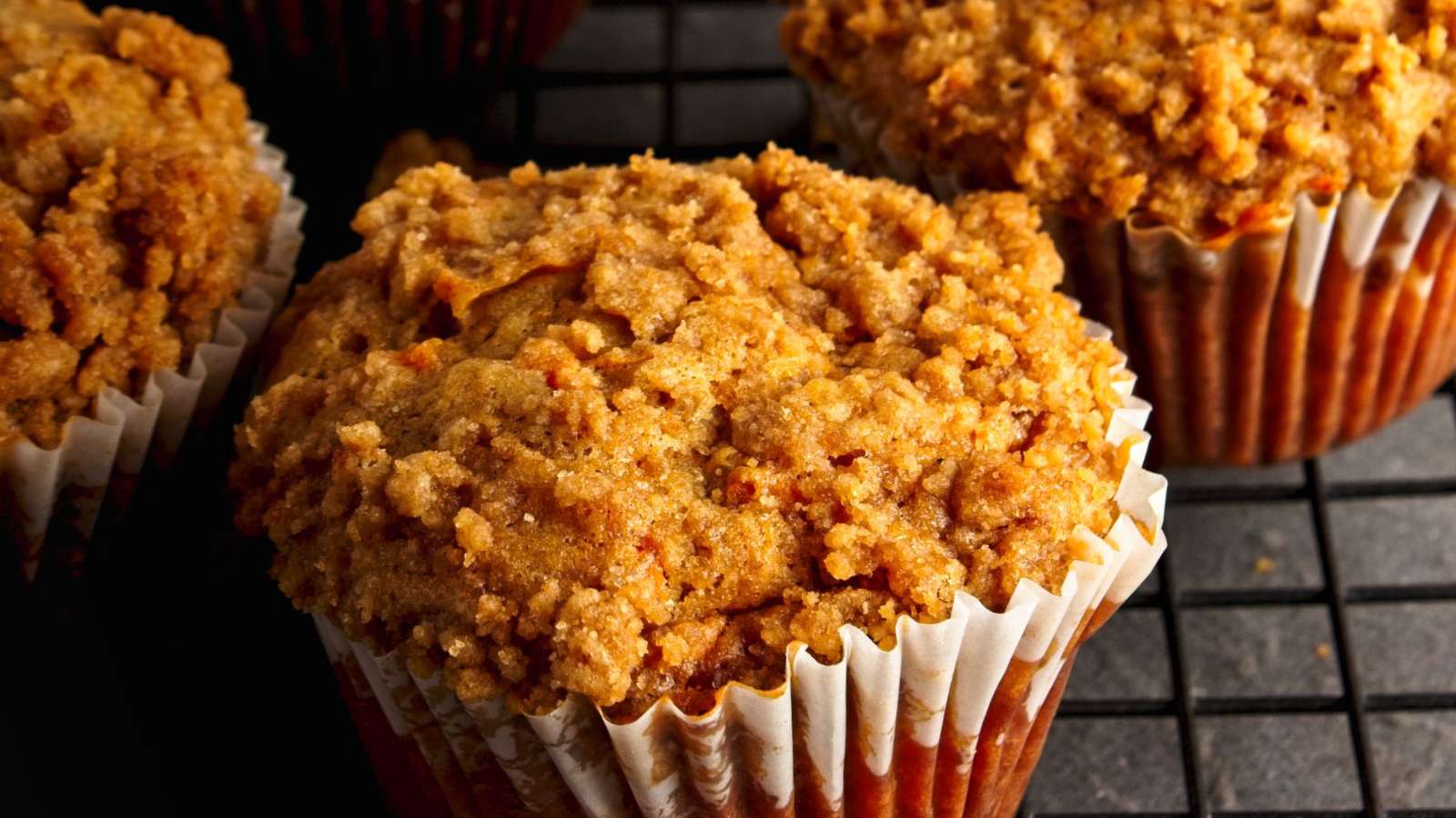 Close-up of muffins with a crumbly streusel topping in white paper liners, cooling on a black wire rack.