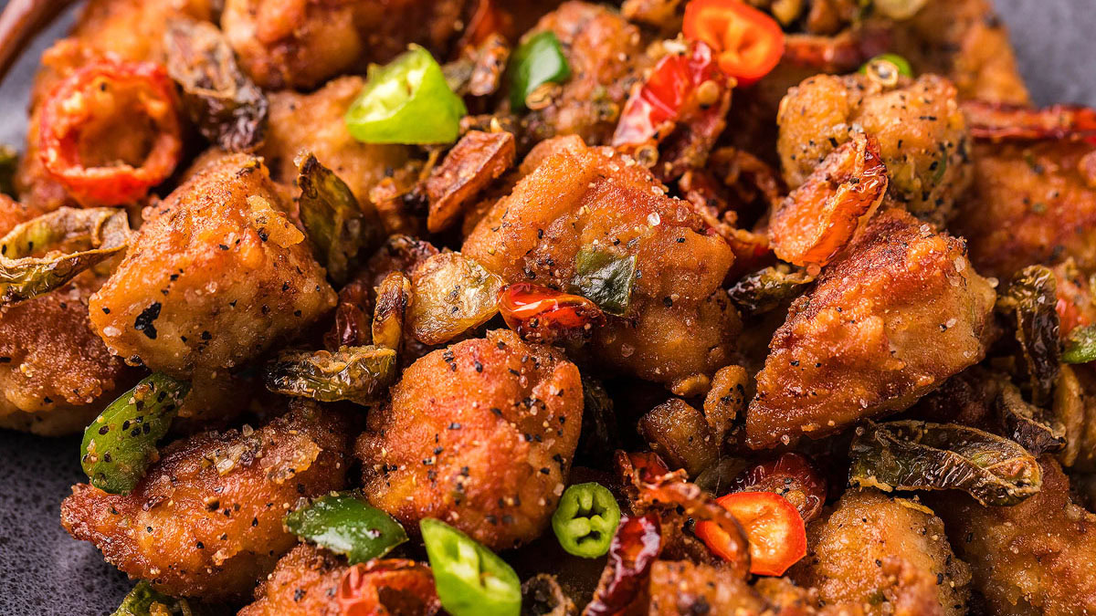 Close-up of crispy fried chicken pieces garnished with sliced green and red chili peppers and herbs.