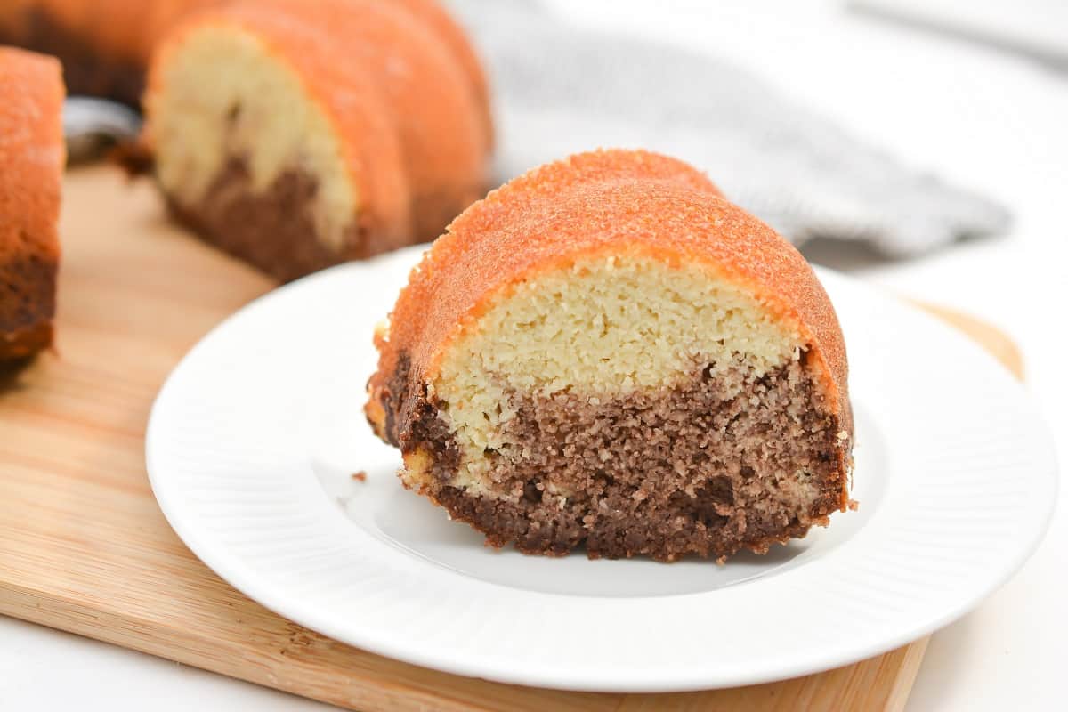 A slice of marble bundt cake with visible chocolate and vanilla layers sits on a white plate.