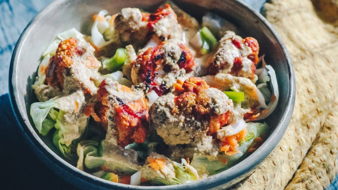 A bowl of salad topped with meatballs, sauce, chopped vegetables, and served with flatbread on the side.