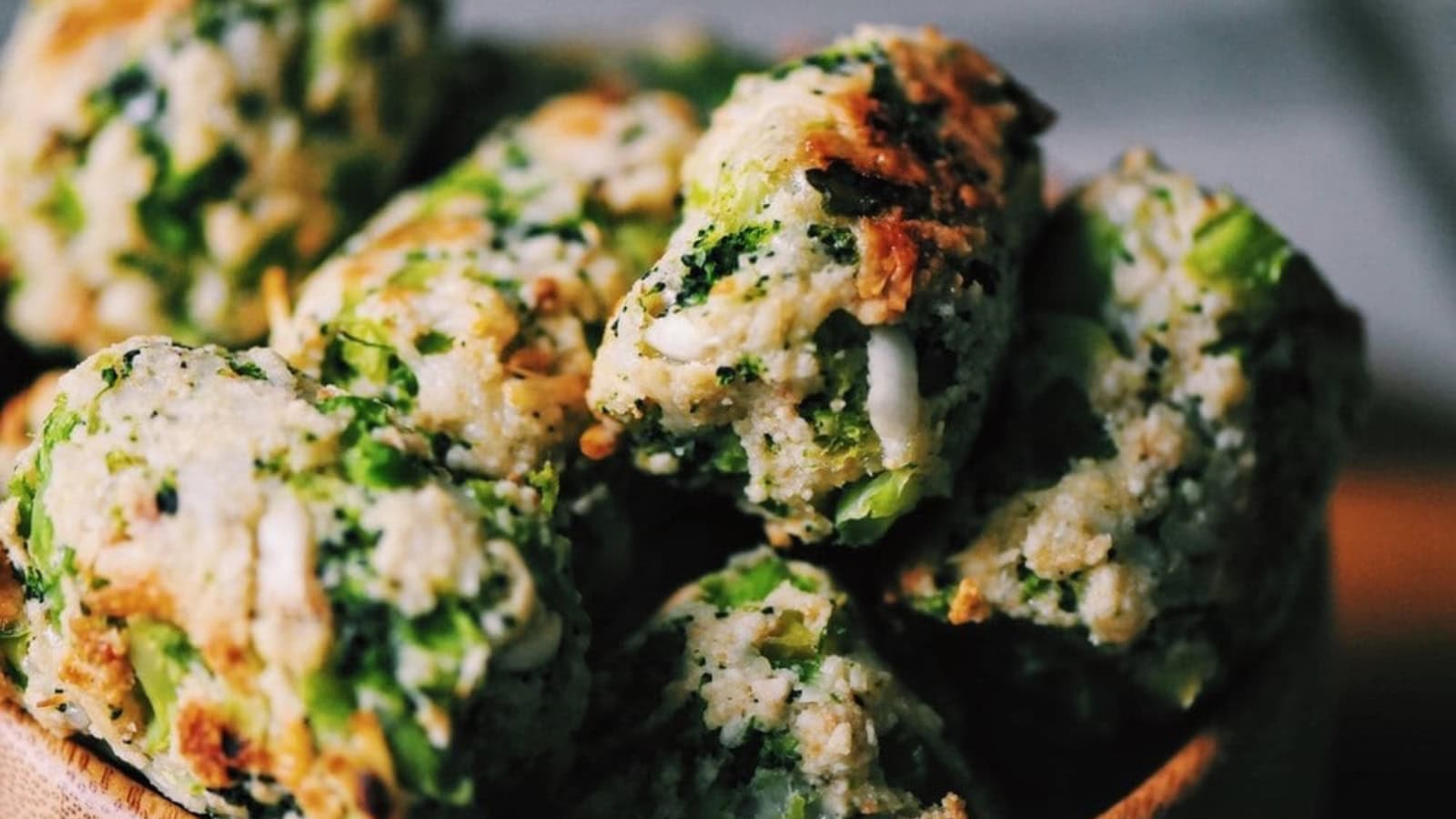 A close-up of several broccoli and cheese tots arranged in a wooden bowl, showing their textured, golden-brown surface.