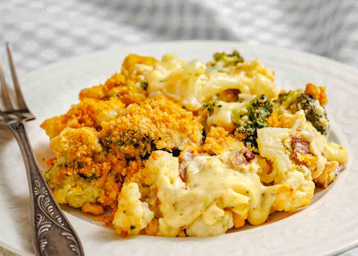 A serving of cheesy broccoli and cauliflower casserole topped with breadcrumbs on a white plate with a fork.
