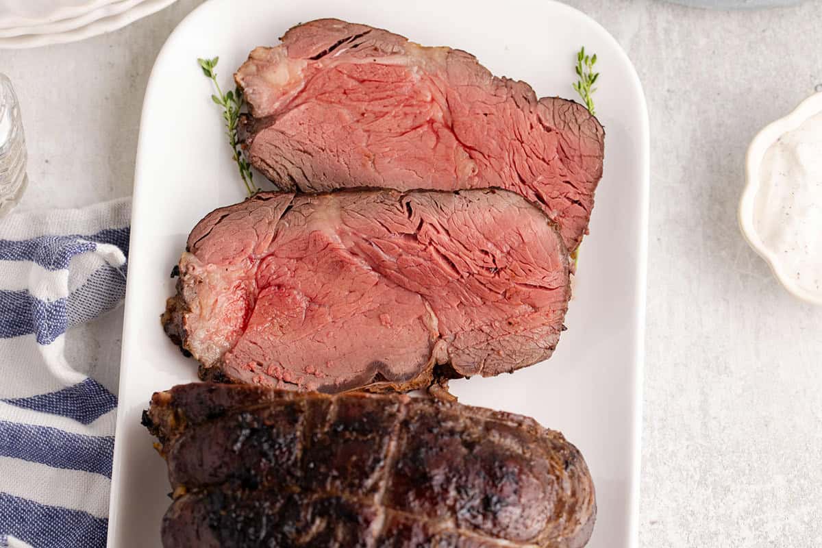 Two thick slices of medium-rare roast beef are served on a white platter, with the rest of the roast nearby.