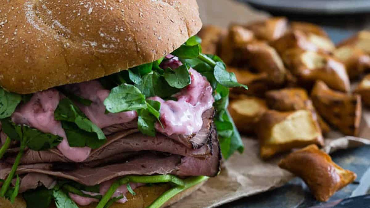 A roast beef sandwich with greens and pink sauce on a whole wheat bun, served with pretzel bites.