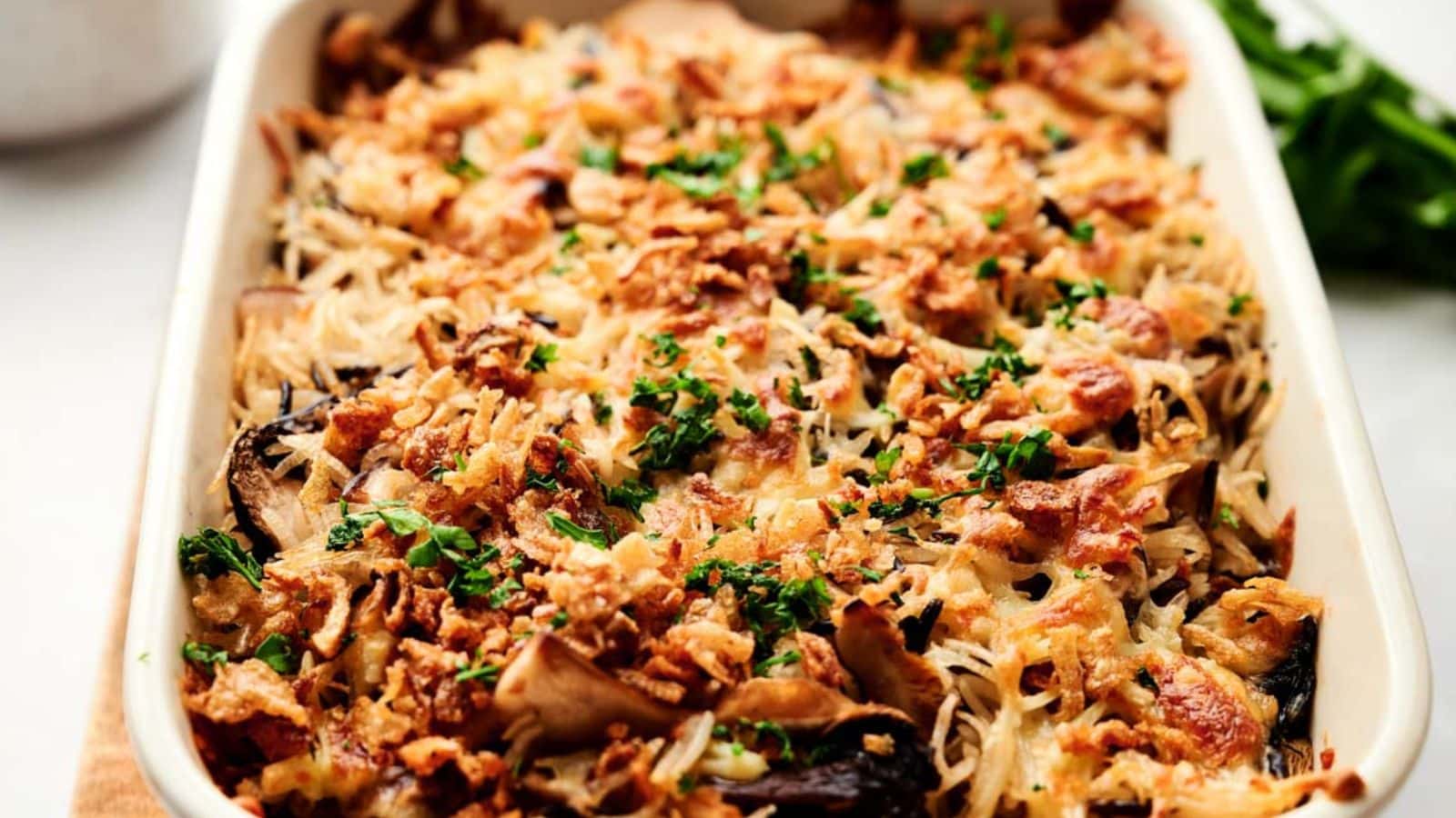 A baked casserole topped with crispy fried onions and chopped parsley, featuring a golden-brown crust and visible shredded pieces, served in a rectangular dish.