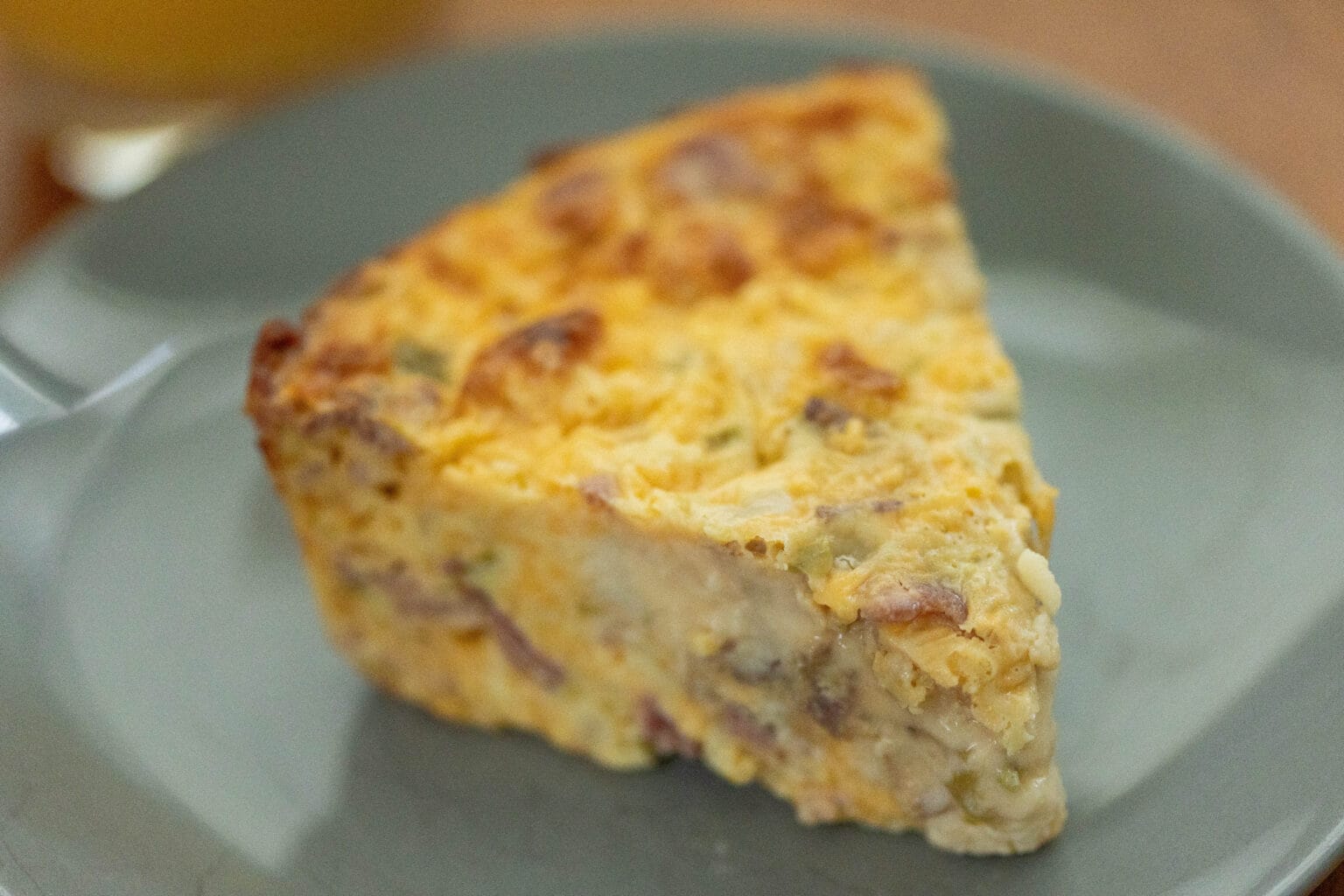A close-up of a slice of baked quiche with a golden-brown top, served on a gray plate.