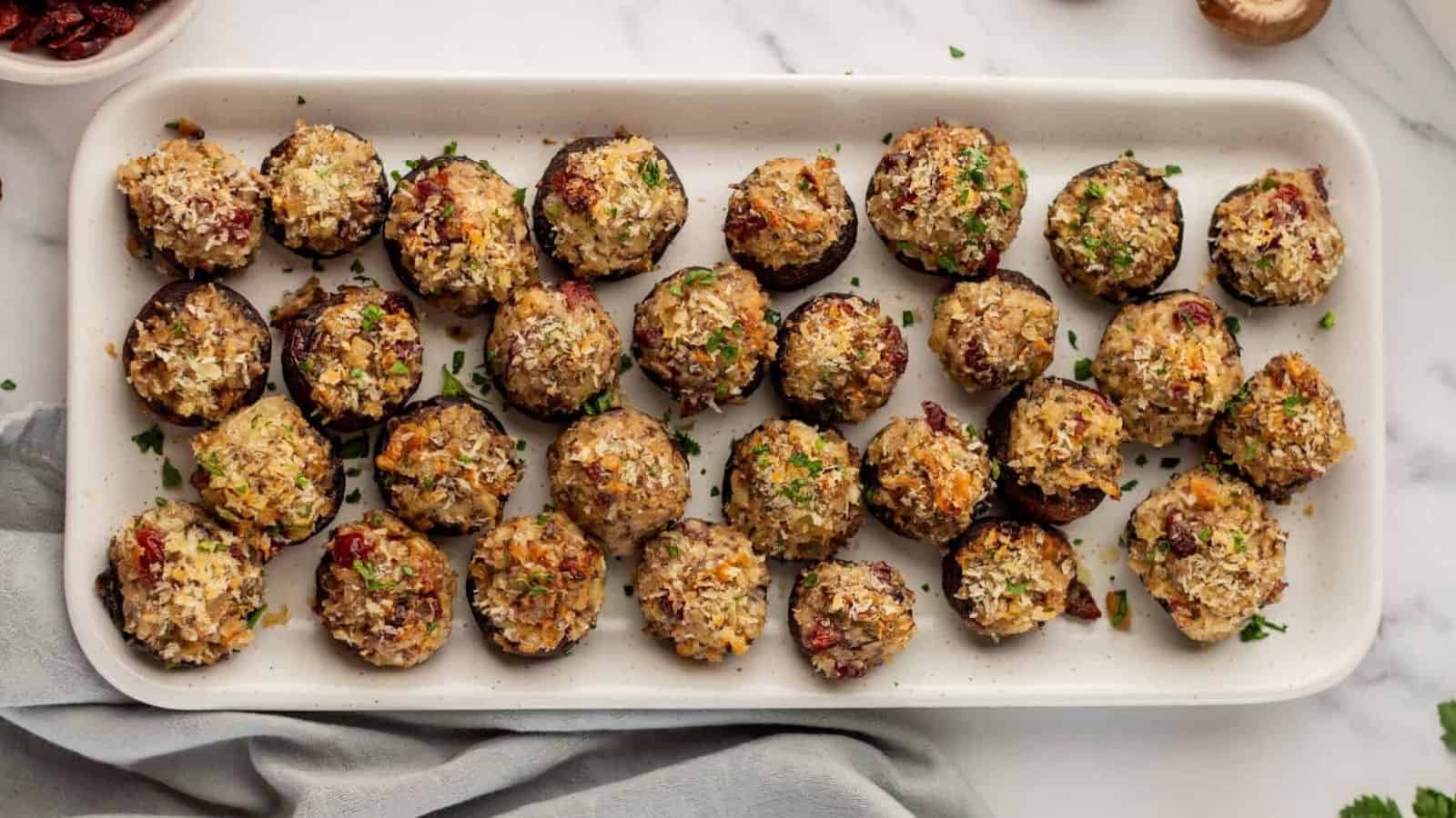 A rectangular white platter filled with evenly arranged stuffed mushrooms, garnished with chopped herbs.