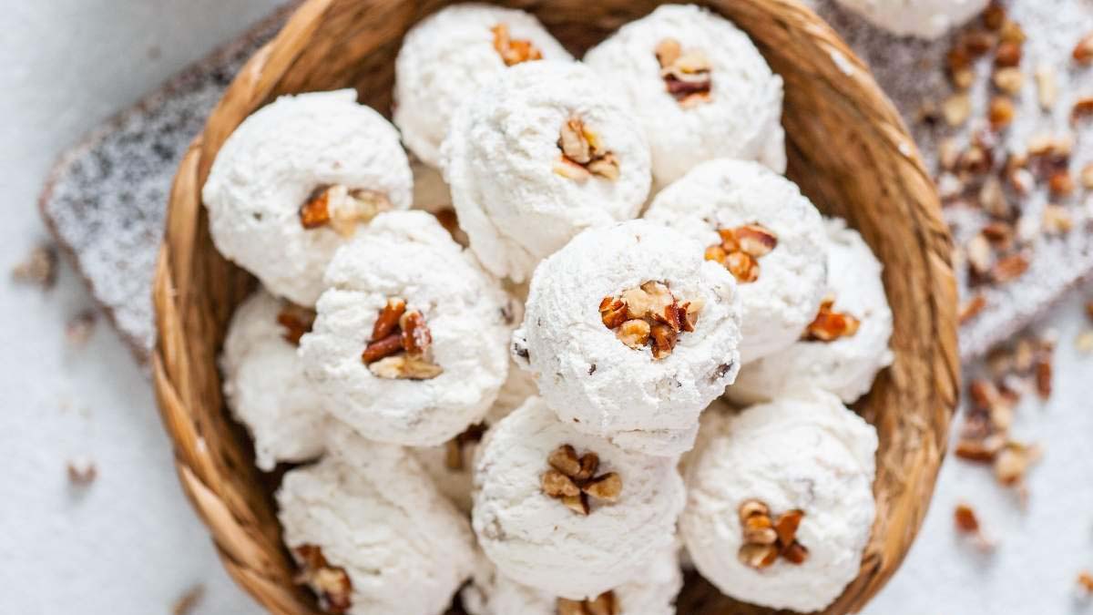 A basket filled with round, white powdered cookies topped with pieces of walnut, with more chopped nuts scattered around.