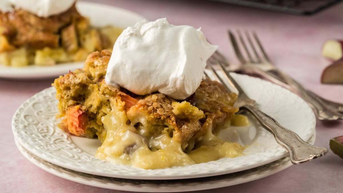 A slice of fruit pie with a golden crust and creamy filling, topped with a dollop of whipped cream, served on a white plate with a fork.