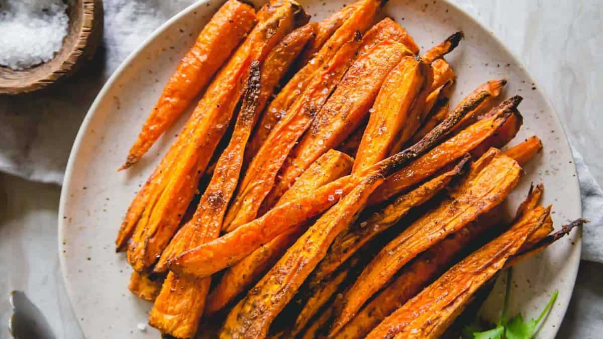 A plate of roasted carrot sticks lightly seasoned with salt, served on a white dish.