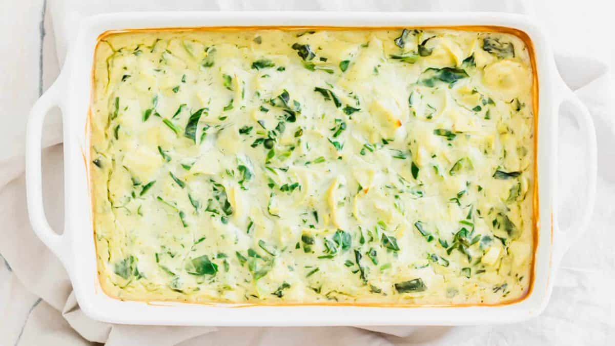 A rectangular white baking dish filled with creamy spinach and artichoke dip, baked until lightly golden around the edges.