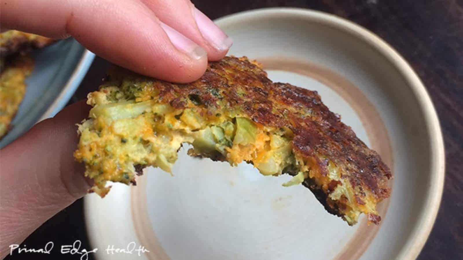 A hand holds a partially eaten vegetable patty over a ceramic plate.