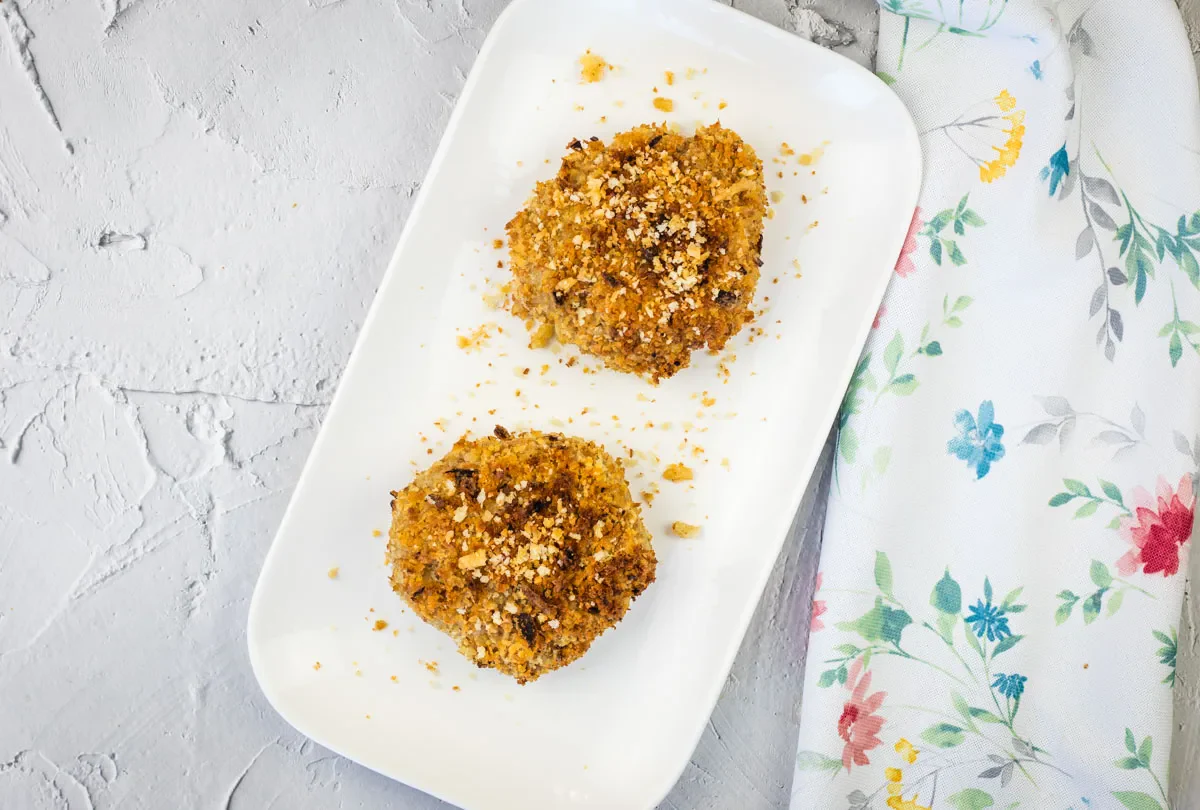 Two breaded and baked patties on a white rectangular plate, placed next to a white napkin with a colorful floral pattern.