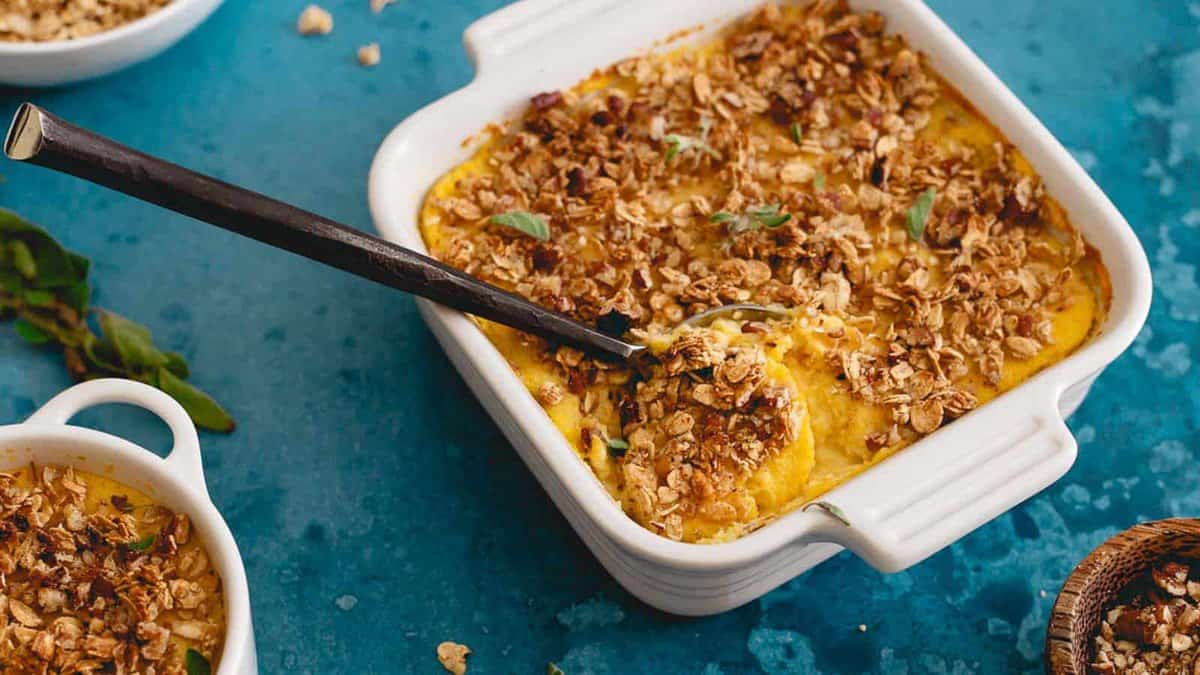 A square baking dish filled with a golden baked fruit crisp topped with oat crumble, with a spoon resting inside.