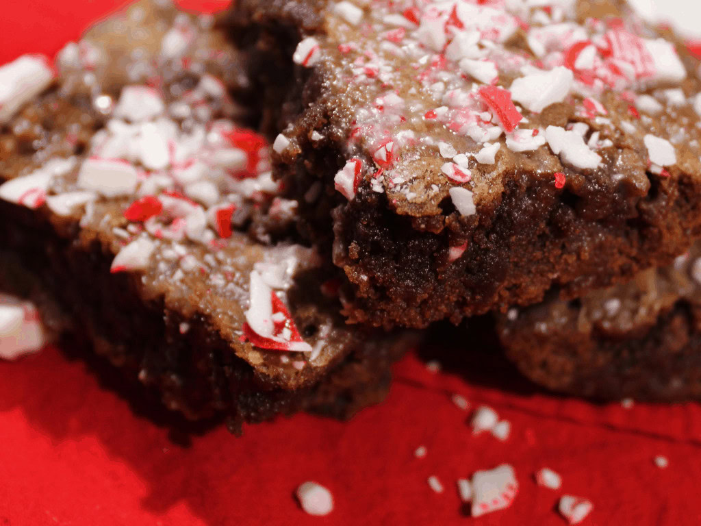 Close-up of brownies topped with crushed peppermint candy, placed on a red surface.