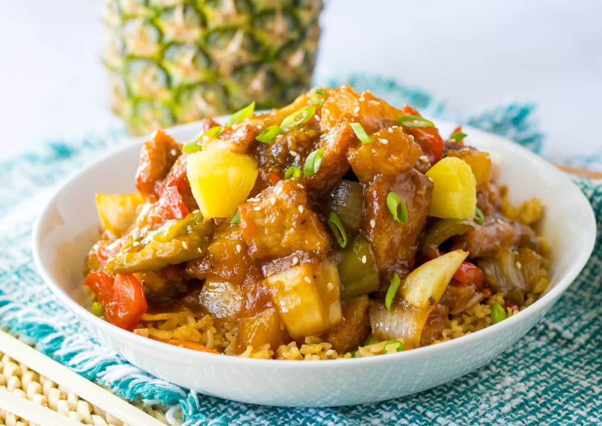 A bowl of stir-fried vegetables and pineapple chunks served over rice, garnished with green onions.