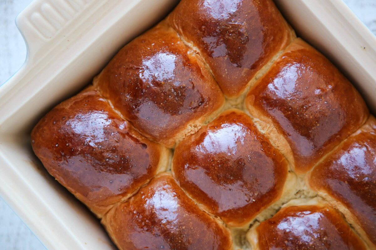 A close-up of eight golden-brown, shiny dinner rolls in a rectangular baking dish.