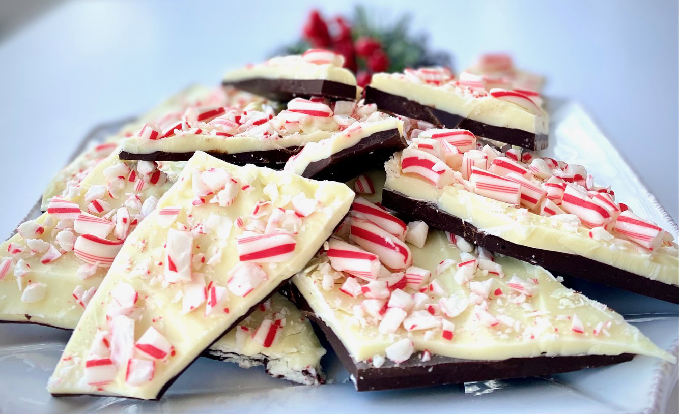 A plate of chocolate bark topped with white chocolate and crushed peppermint candy pieces is arranged on a platter.