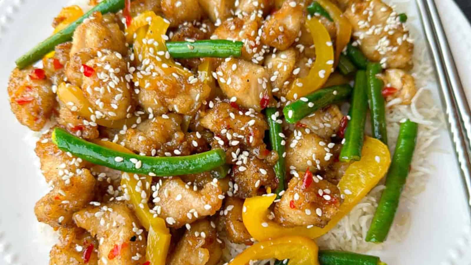 Stir-fried chicken with yellow bell peppers, green beans, and sesame seeds served over white rice on a white plate.