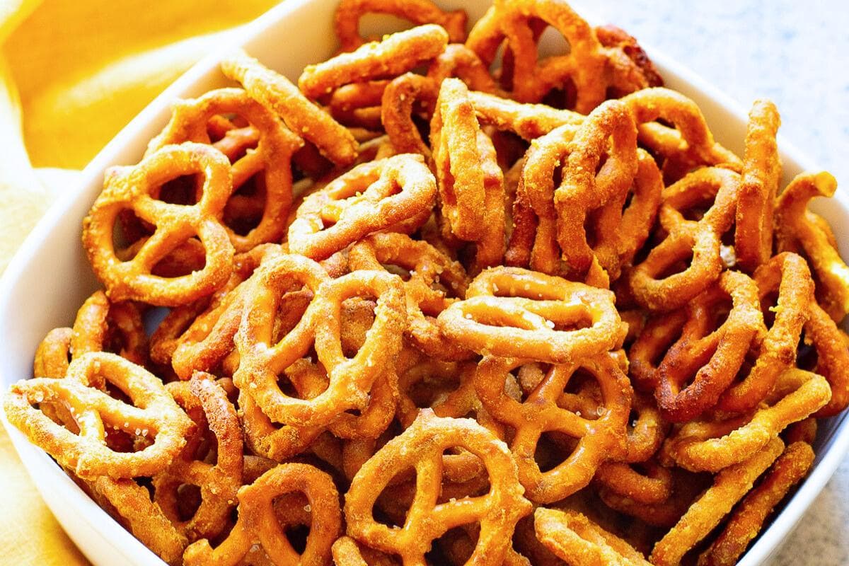 A white bowl filled with seasoned, crispy pretzel twists arranged closely together.
