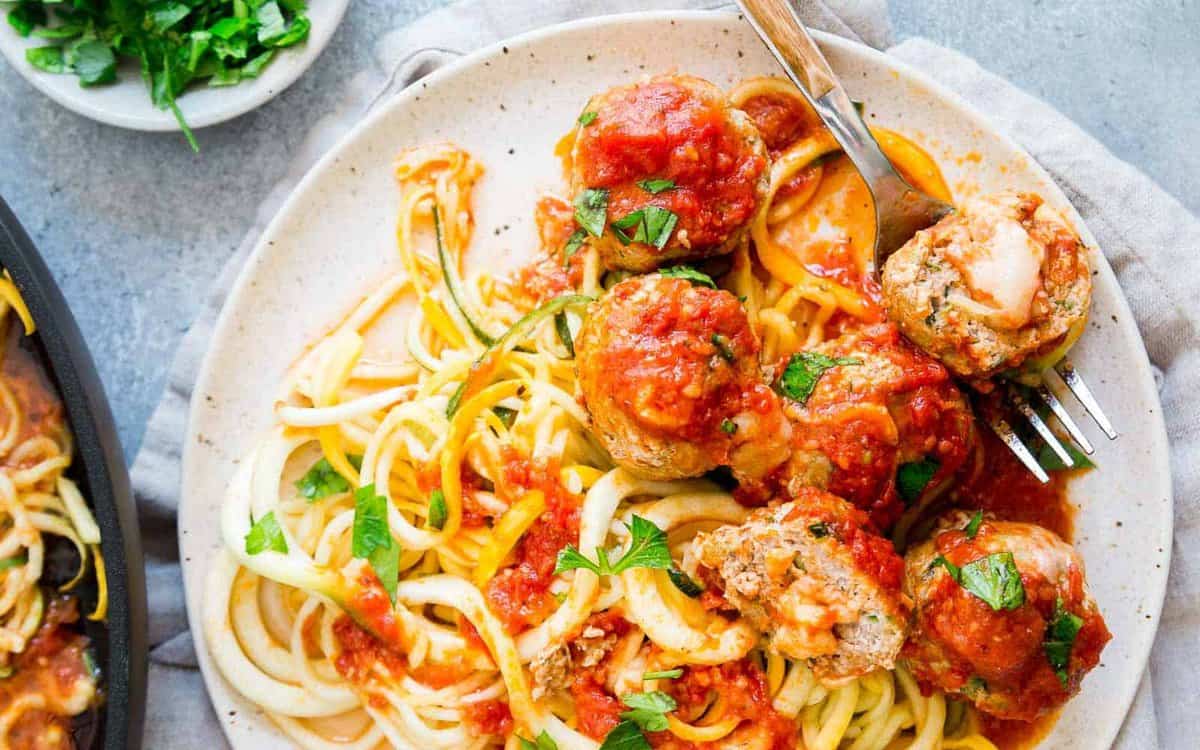 A plate of spiralized vegetable noodles topped with meatballs, tomato sauce, and chopped parsley, with a fork resting on the plate.