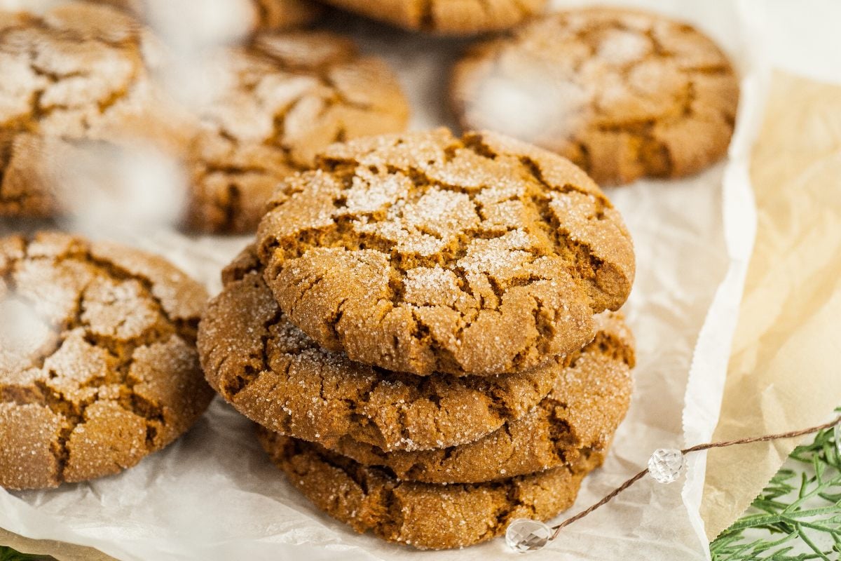 A stack of three sugar-coated ginger cookies sits on parchment paper, with more cookies in the background.