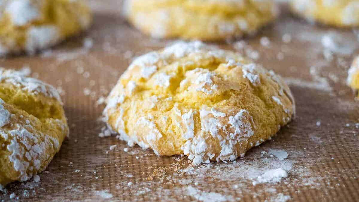 Golden, round cookies dusted with powdered sugar rest on a brown baking sheet.