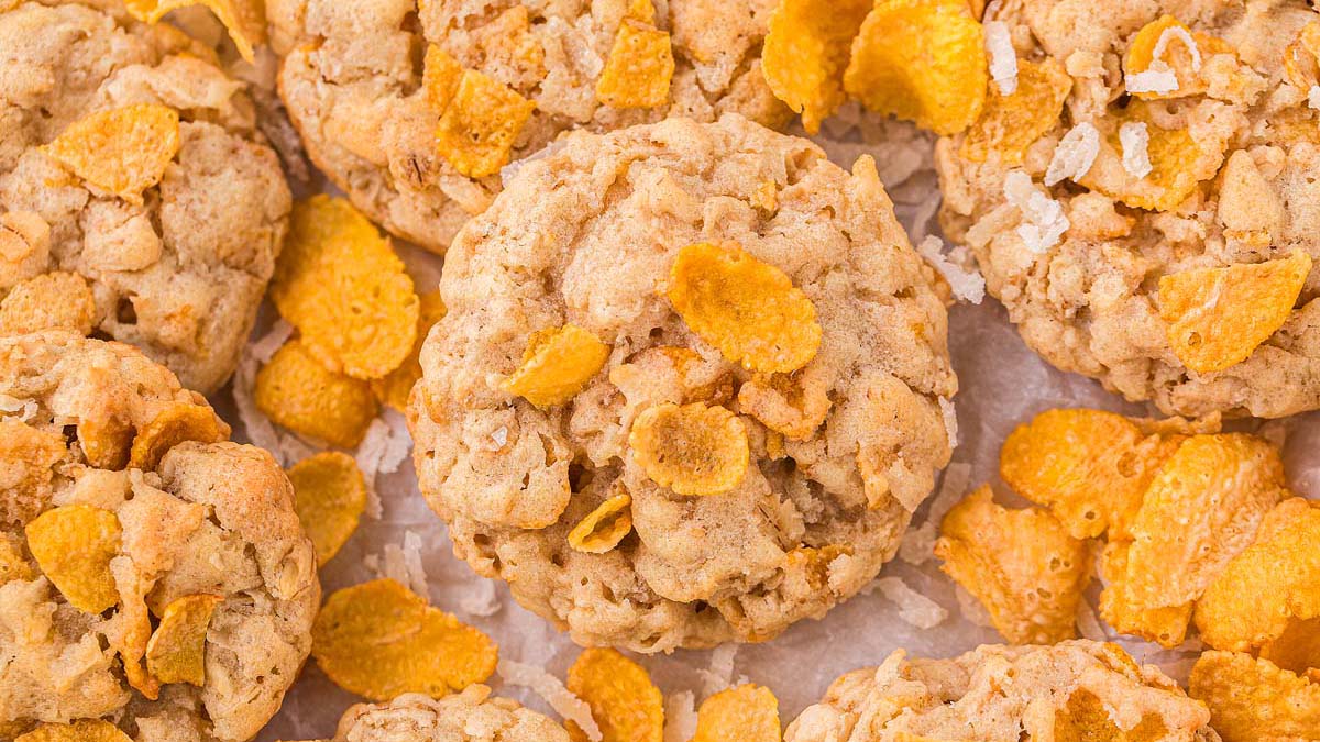 Close-up of several round cookies mixed with cornflakes, displayed on a light-colored surface.